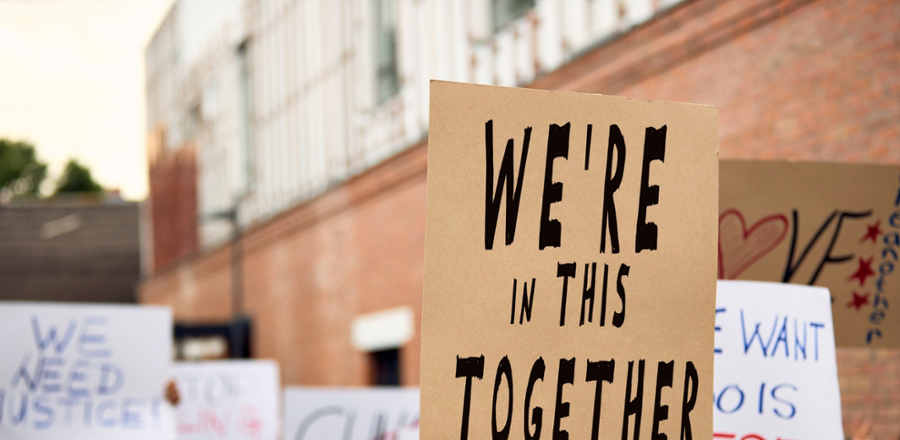 Variety of picket signs with text on prominent sign. "We're In This Together"