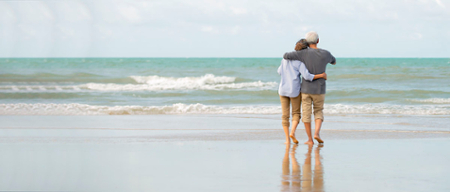 Older couple walking on beach toward ocean horizon